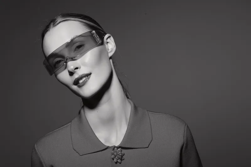 Elegant Asian woman with light skin wearing stylish translucent sunglasses and textured top poses in black and white studio portrait. Concept of fashion and modern beauty.