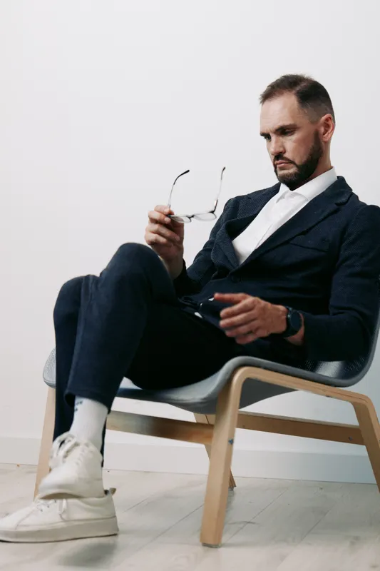 A man in business attire sits thoughtfully, isolated against a colored background, conveying a professional mood and subtle emotions of focus and contemplation.