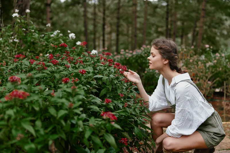 Romantic young woman in white blouse enjoying flowers in a lush garden, capturing the essence of nature and tranquility