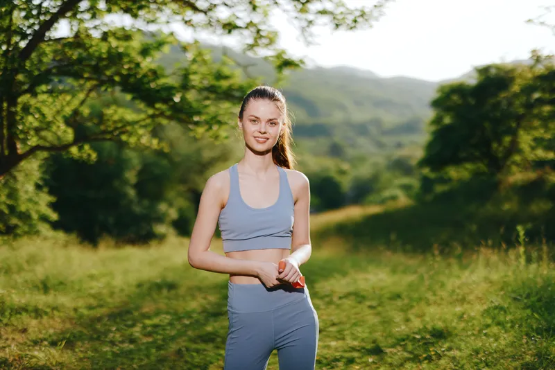 Young athletic woman in activewear smiling in nature, healthy lifestyle concept, green background, sunlight, athletic fitness, outdoor exercise