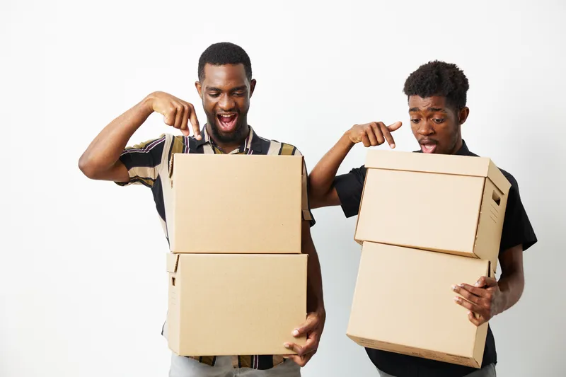 Excited black men unpacking boxes, showcasing surprise and joy. Two friends sharing a moment together, highlighting friendship and discovery in a vibrant setting.