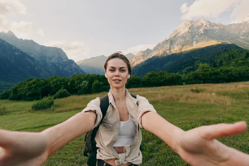 Nature, outdoors, hike, woman, landscape, a woman on a scenic hike extends arms toward the camera in a lush valley with mountains, conveying freedom and a deep connection to nature.
