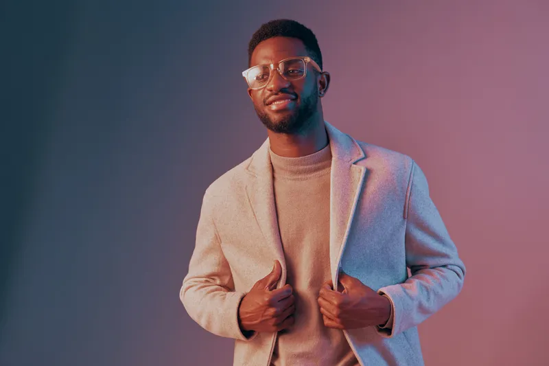 Confident young man in stylish outfit with glasses, smiling against a colorful gradient background, showcasing modern fashion and positive energy