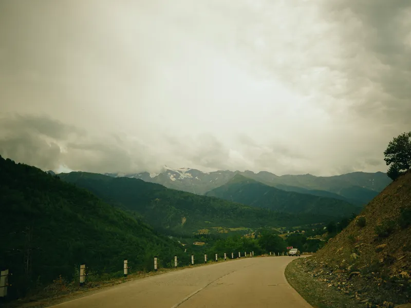 Winding road through rugged mountains offers a sweeping landscape under a muted, cloudy sky, with guardrails along a scenic valley, inviting exploration and outdoor travel.