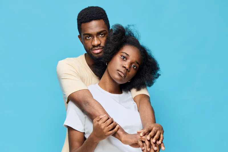 A couple embracing in front of a blue background, expressing love and connection, showcasing diversity and modern fashion