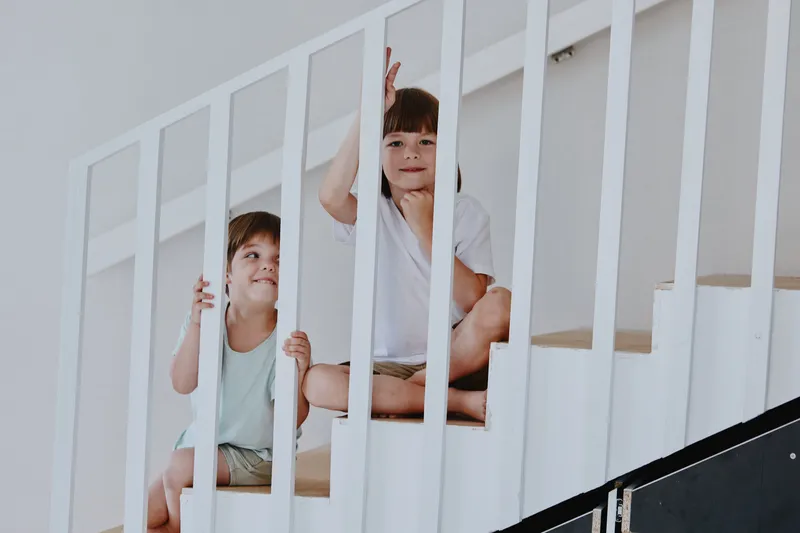 Two playful children enjoying time together at home, one boy and one girl, sitting on the steps and smiling, creating a cheerful atmosphere.