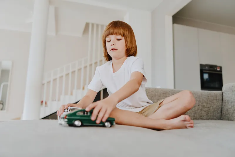 Young boy playing with toy cars, sitting on a cozy sofa in a modern living room, showcasing imagination and creativity in a relaxed environment.