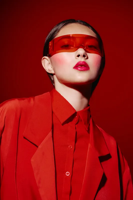 Fashion portrait of a young woman with red lips and orange visor sunglasses wearing vibrant red clothing on a red background. Concept of beauty creative fashion studio look.