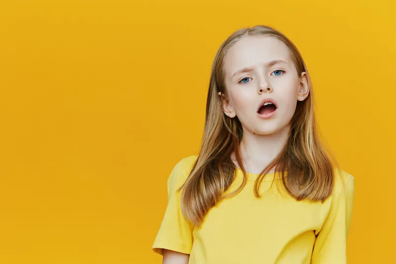 Portrait of a young girl expressing surprise against a vibrant yellow background, wearing a bright yellow shirt with medium length hair and a playful demeanor