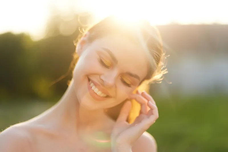 Young woman enjoying a sunny day outdoors, smiling gently with a warm glow, embodying happiness, summer vibes, and natural beauty in a serene environment