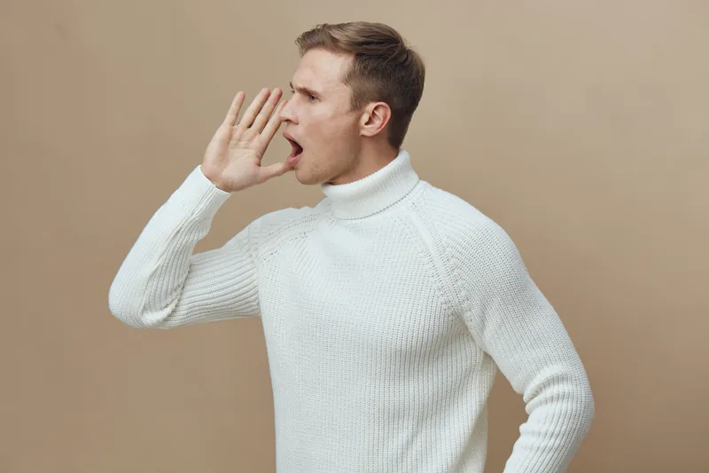 Young caucasian man in white sweater shout hold hand near mouth side view isolated on beige background digital detox mental health concept