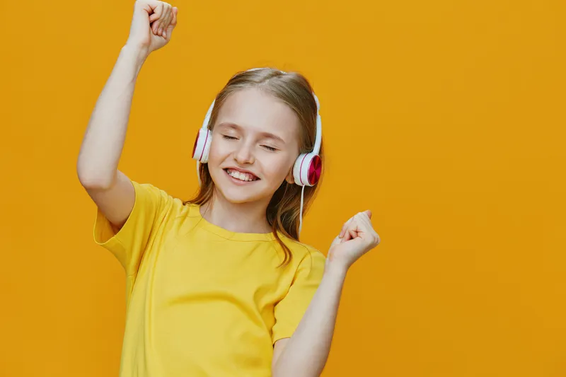 Happy girl dancing with headphones on a vibrant yellow background, expressing joy and freedom through music and movement while wearing a cheerful yellow T shirt