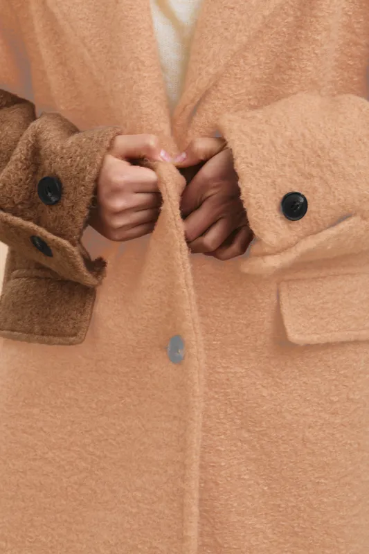 asian woman wearing a tan coat is seen adjusting buttons in a close up shot, presenting a warm, stylish look with rich fabric texture and poised confidence.
