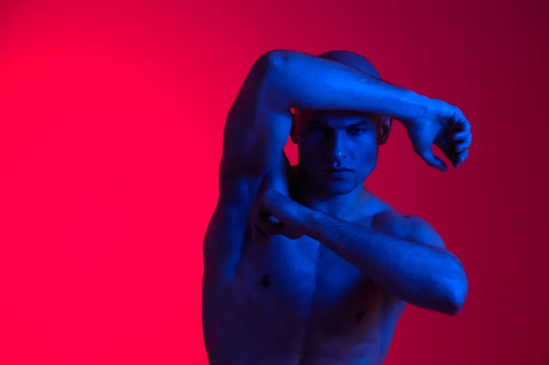 A striking portrait of a man posing dramatically, highlighting the interplay of blue light against a vibrant red background. This image captures emotion and artistry beautifully.