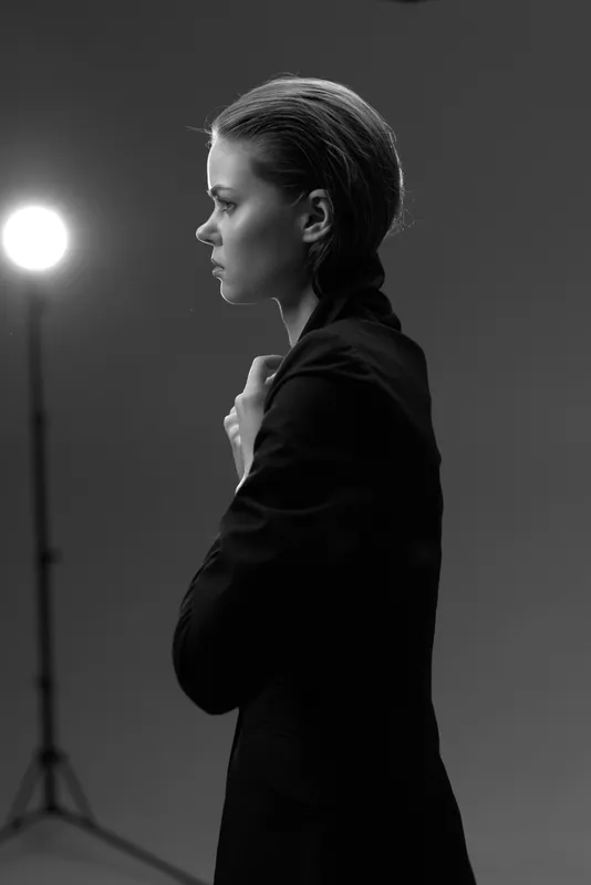 Black and white portrait of a thoughtful woman in a dark blazer with dramatic lighting and studio background