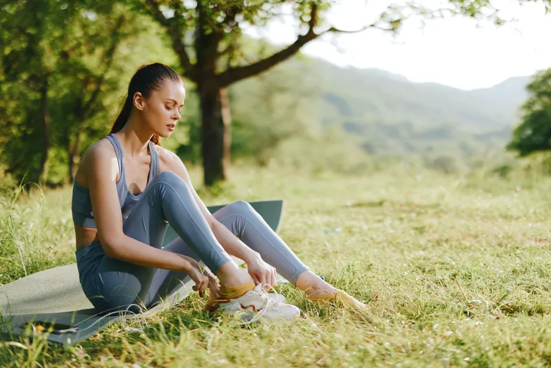 Young athletic woman tying shoelaces in a serene outdoor setting, wearing activewear in soft pastel colors, embodying focus and determination while preparing for a workout