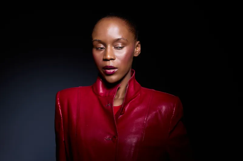 Portrait of elegant dark skinned African woman wearing a red leather jacket with high collar, isolated on black background. Concept of fashion, beauty, confidence, and style.