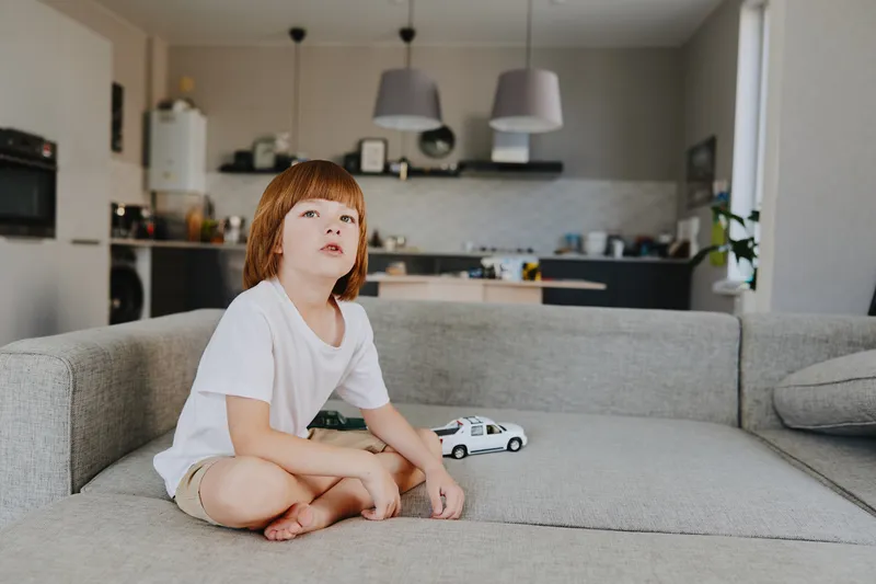 Curious boy sitting on a cozy sofa, playing with toy cars in a modern living room, surrounded by a warm atmosphere and stylish decor.