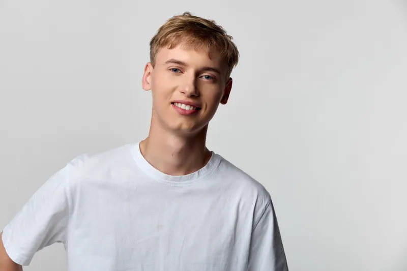 Young man in a white tee smiles in a bright studio with a relaxed vibe, simple backdrop and clean lighting for a casual, friendly feel.