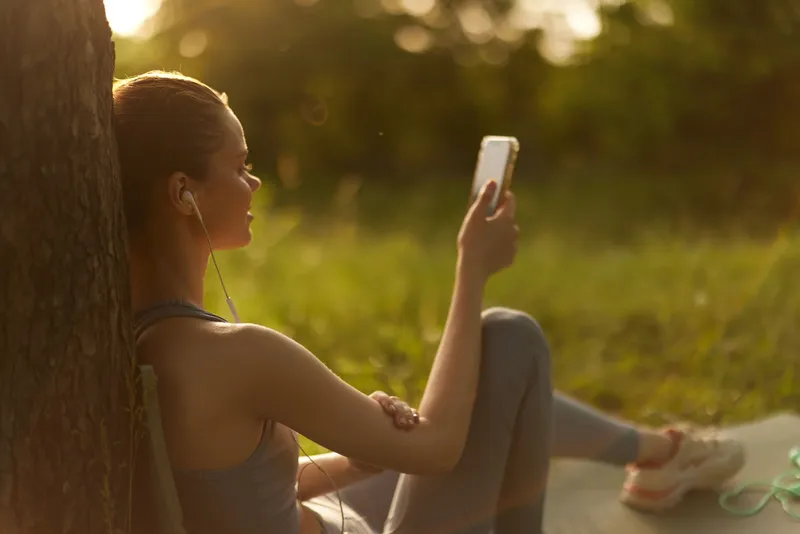 Young woman enjoying music on her smartphone in a serene outdoor setting, wearing athletic clothing, capturing a moment of relaxation and happiness