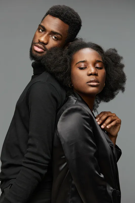 Elegant portrait of a Black couple with stylish attire, showcasing intimacy and sophistication against a grey background, perfect for romantic or fashion themed projects