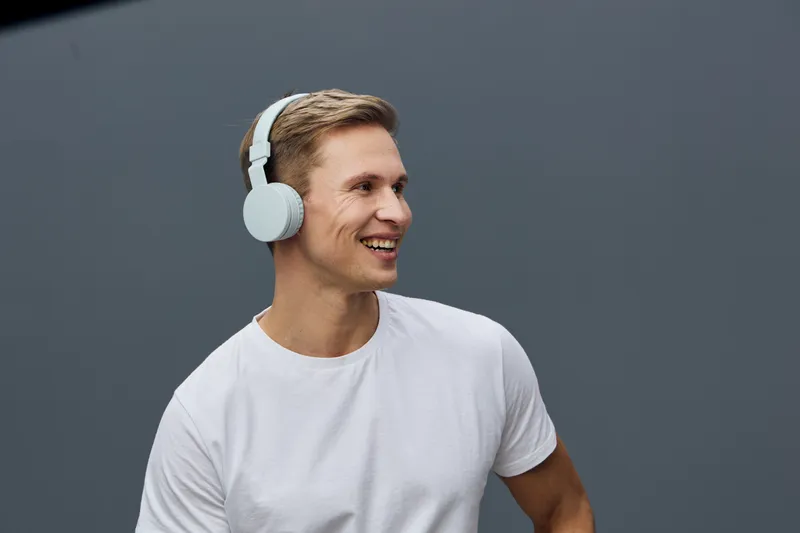 smiling man wearing white headphones and plain t-shirt enjoy digital detox against gray background casual style
