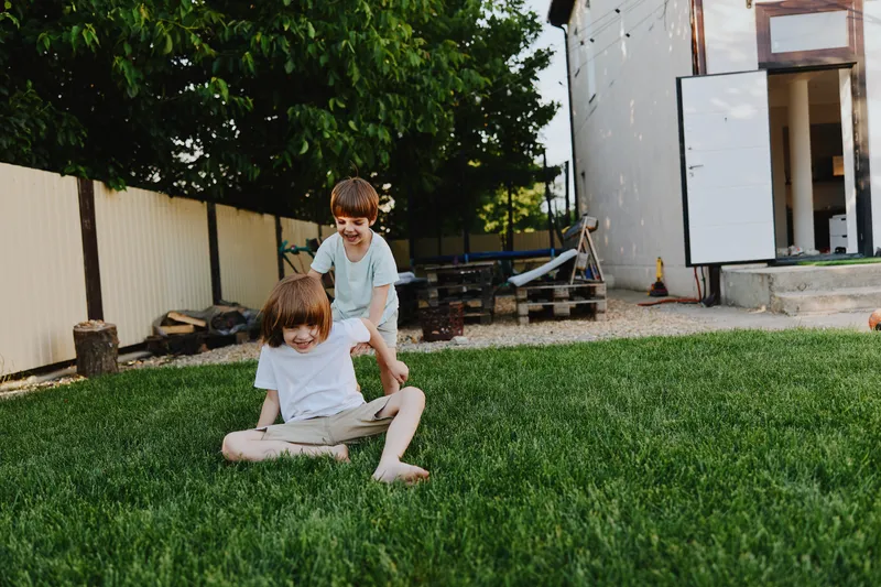 Joyful children playing on grass, enjoying outdoor fun in a sunny backyard with lush greenery and playful energy. Perfect for family moments and childhood memories.