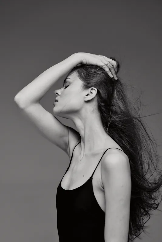 Black and white portrait of a woman with long hair posing gracefully in a black top against a neutral background