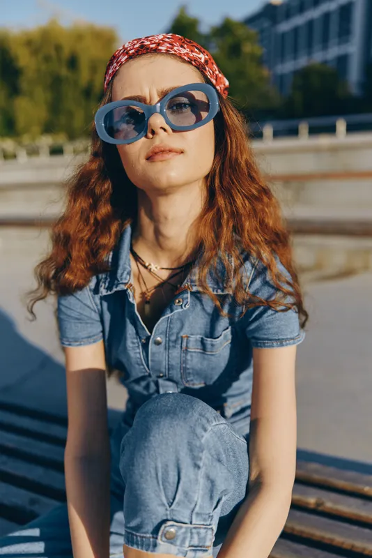lifestyle woman in modern boho-western denim street style wearing oversized sunglasses and a red printed headband, captured with warm film color tones outdoors
