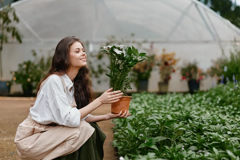 Young woman holding a potted plant in a greenhouse, showcasing joy and connection with nature, in a vibrant green setting, embodying the concept of healthy living and gardening