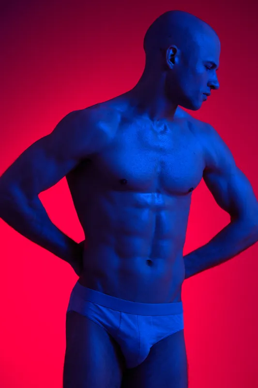 Athletic man posing dramatically, showcasing toned physique under vibrant blue lighting, emphasizing strength and artistry. Ideal for fitness or lifestyle concepts.