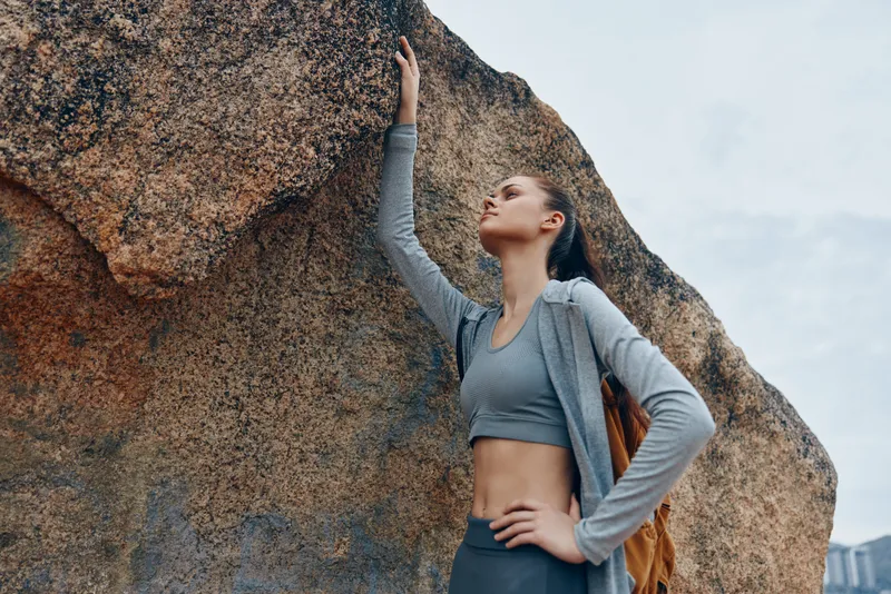 Athletic young woman in sportswear climbing rocky terrain, expressing determination and strength in a natural outdoor setting
