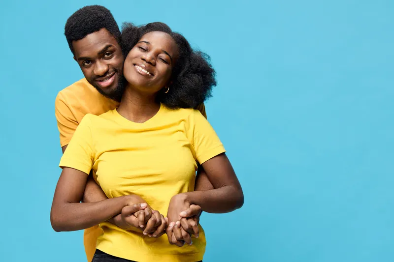 Happy young couple embracing, wearing matching yellow shirts, on a vibrant blue background, conveying love and joy in a cheerful atmosphere