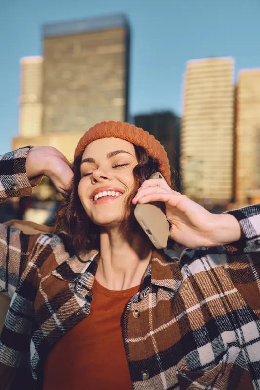 woman smile phone city beanie plaid sunlight joyful candid lifestyle portrait of a woman on phone at golden hour glow, authenticity and emotional storytelling with mindful living warmth