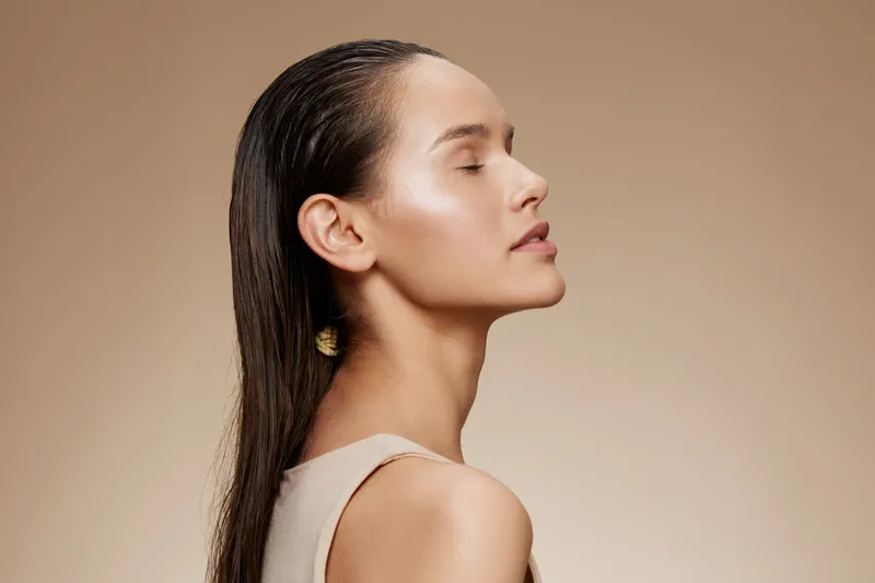 Elegant woman with long hair in a neutral outfit, gazing upwards, conveying serenity and self confidence against a soft beige background