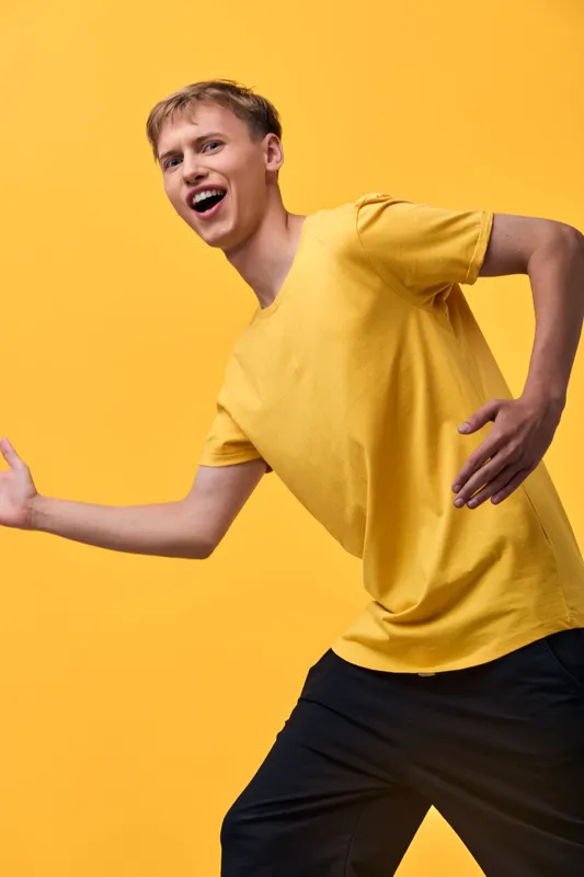 Energetic youth dancing in a bright yellow backdrop, showcasing dynamic movement, laughter and casual fashion in a lively studio vibe