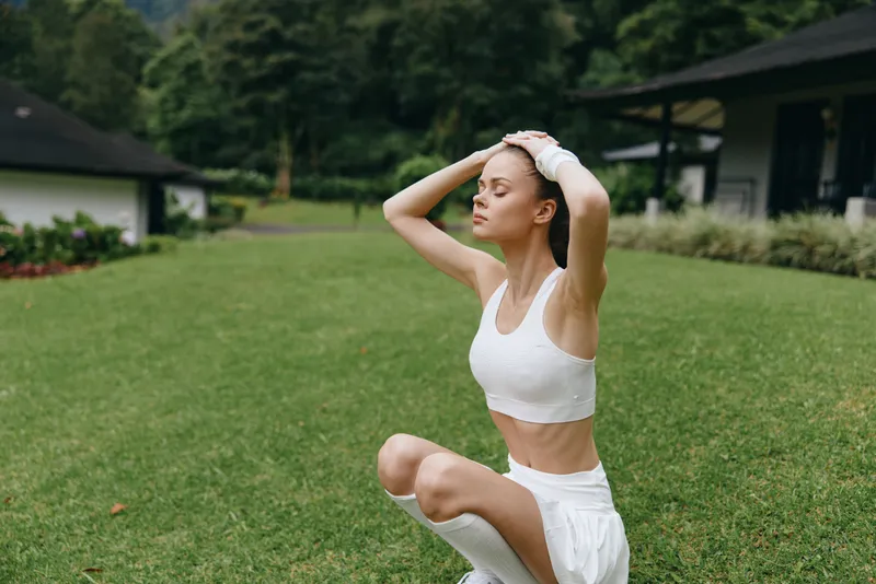Young woman in athletic wear practicing mindfulness outdoors in a lush green park, promoting healthy lifestyle and relaxation during fitness activities