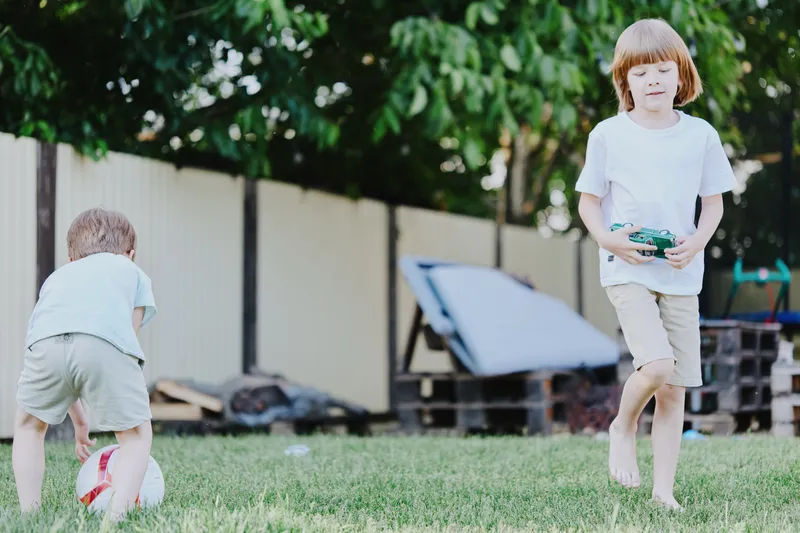 Active boys playing with a ball in the garden, enjoying the sunny day and vivid green grass. Perfect scene for capturing childhood joy and outdoor activities. ###