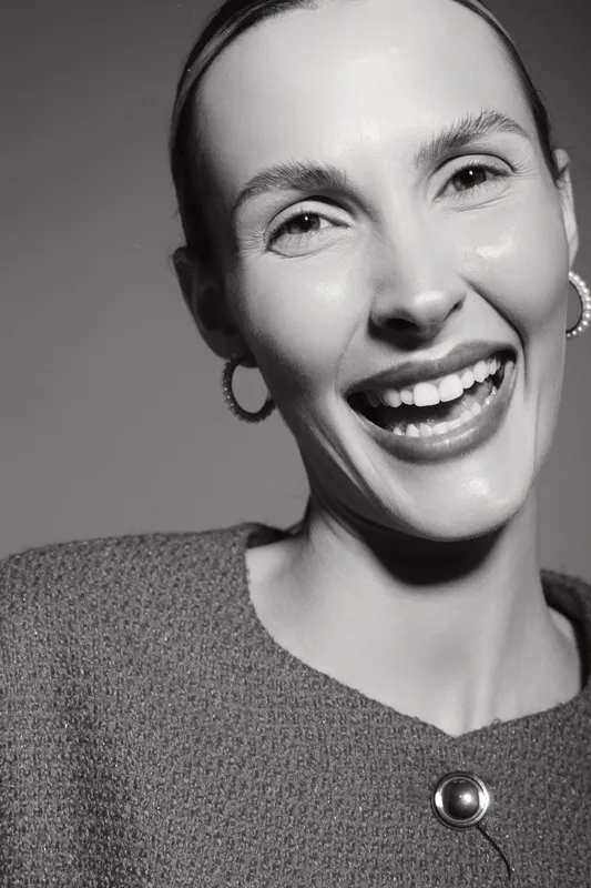 Smiling caucasian woman with fair skin and earrings laughs joyfully wearing textured sweater in black and white studio portrait. Concept of happiness and positive emotions.
