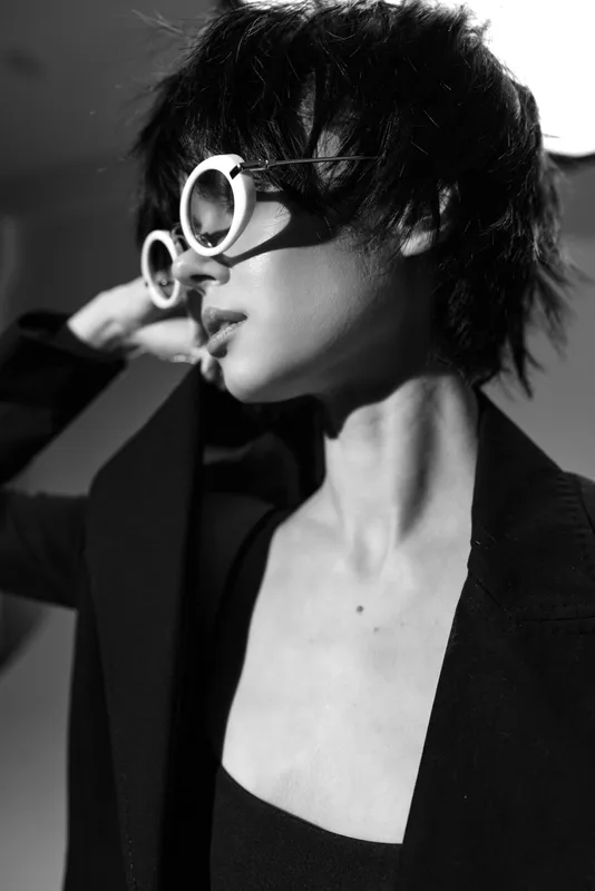 Stylish woman wearing large round sunglasses in black and white portrait with dramatic lighting and modern fashion look