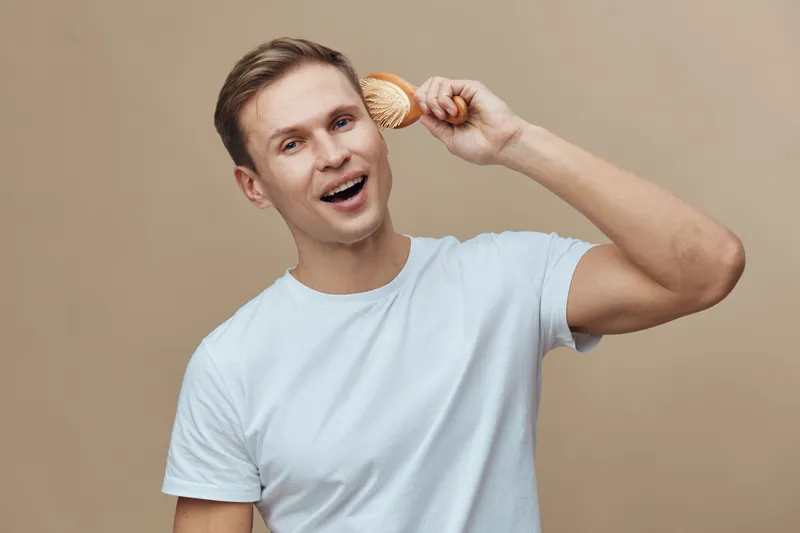 smiling young caucasian man wear white t-shirt hold wooden hairbrush near head isolated on beige background mental health concept