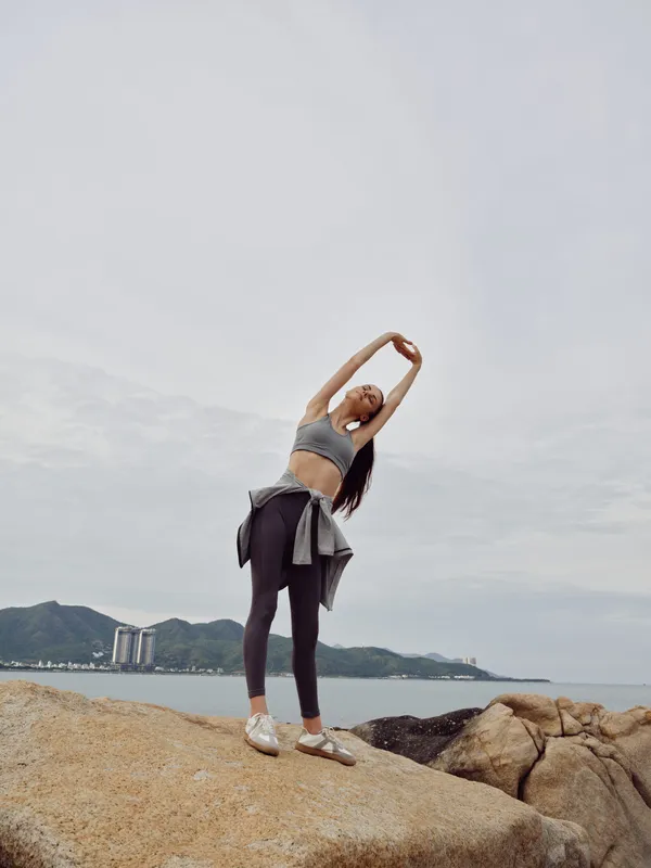 Young woman stretching on rocky beach in athletic wear, embracing fitness and wellness with a serene ocean backdrop