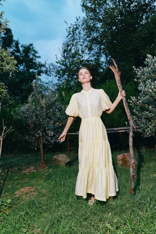Woman portrait in long yellow dress outdoors in nature with authenticity inclusivity, standing in meadow holding rustic stick for fashion mood