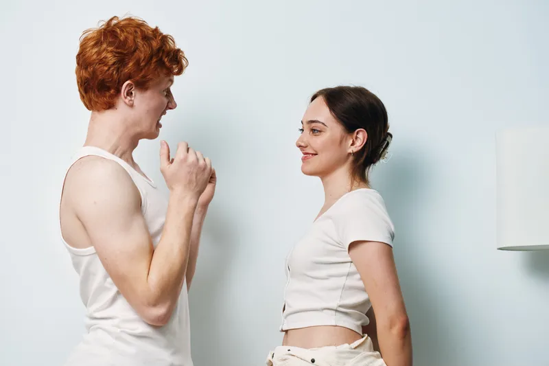 Young man and young woman facing each other with happy expressions in casual clothes against light background. Positive energy, communication and interaction between smiling friends.