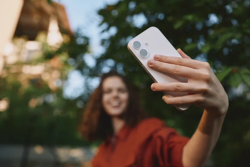 A young woman with brunette hair takes a casual selfie outdoors in a brown top, capturing a candid moment of everyday life and self expression