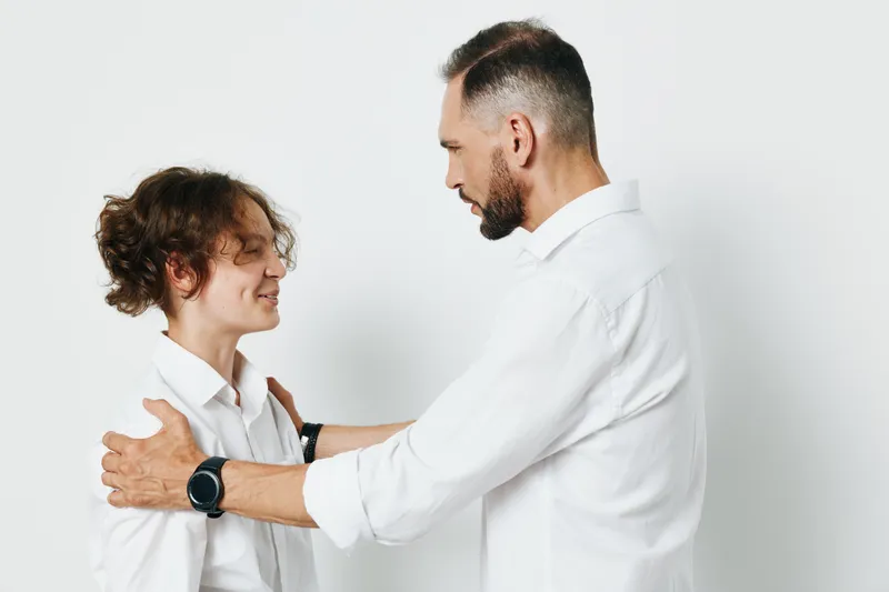 A professional man and colleague share a warm moment against a solid white background, conveying confidence, leadership, and supportive teamwork in a business setting.