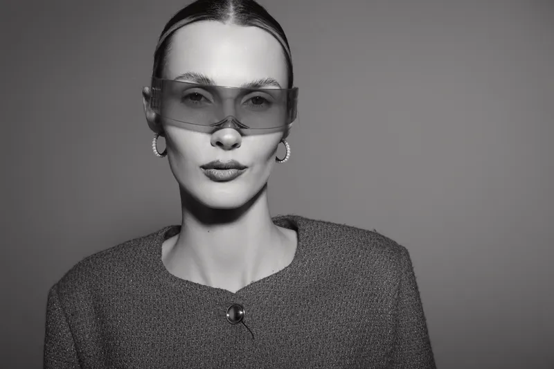 Elegant Caucasian woman with pale skin wears oversized transparent sunglasses and textured jacket, posing confidently in studio. Concept for fashion, style, and glamour portrait.