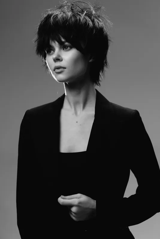 Stylish black and white portrait of a young woman with short hair wearing a dark blazer, showing confident and thoughtful expression.