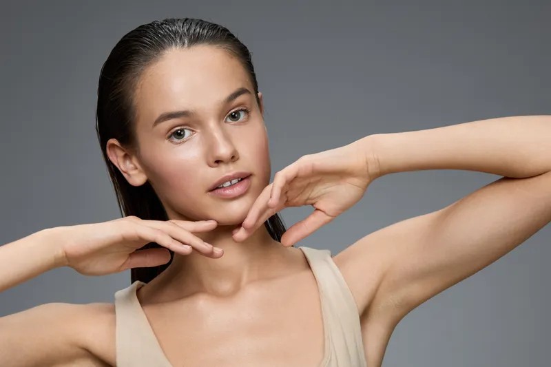 Young woman with natural beauty, clear skin, and wet hair, exuding confidence and serenity in a minimalistic grey backdrop