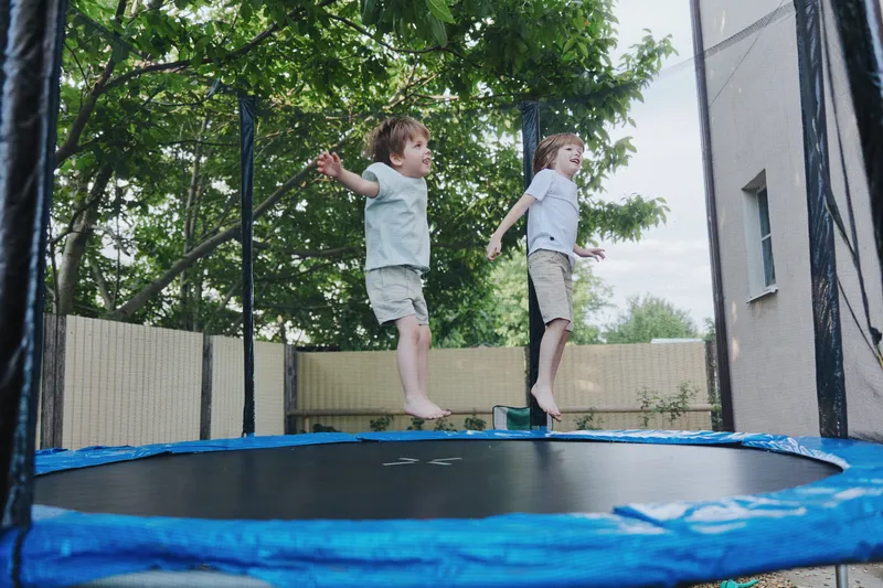 Happy children jumping on a trampoline, playing outdoors in a vibrant garden setting. The scene captures joy, laughter, and the spirit of childhood fun.